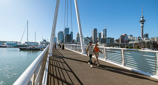 Ein Pärchen schlendert Hand in Hand auf einer Brücke in Auckland bei Sonnenschein